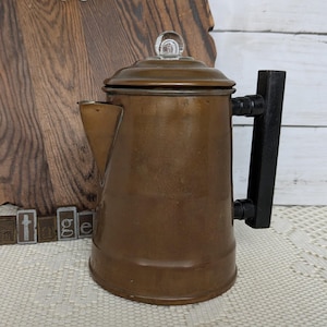 May include: A vintage copper coffee pot with a black handle and a glass knob on the lid. The pot is set against a wooden background shaped like a state. The word "vintage" is spelled out in individual letter blocks.