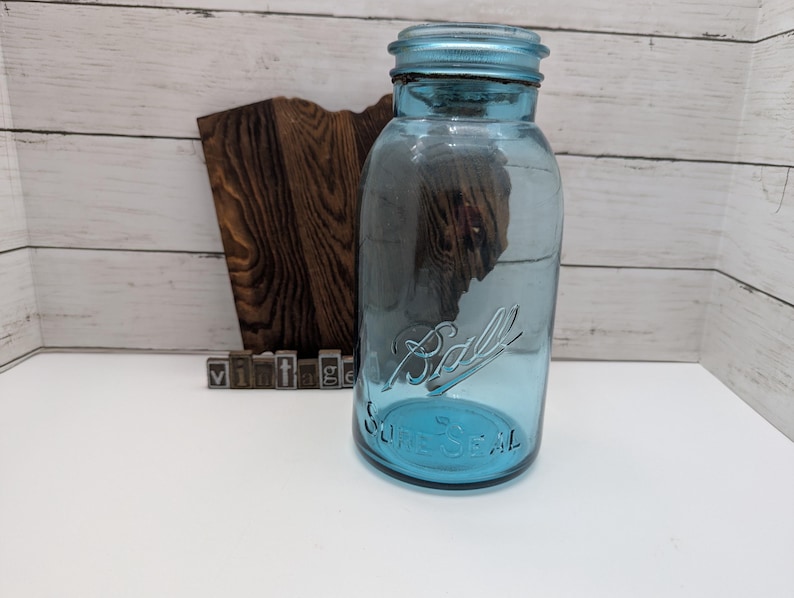 May include: A vintage blue Ball SureSeal mason jar. The jar has a screw-on lid and embossed lettering. The word "Ball" is written in cursive on the front of the jar. The word "vintage" is spelled out in individual metal letter blocks.