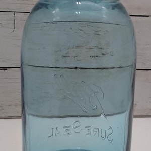 May include: A vintage blue glass jar with a matching lid. The jar has a wide mouth and a rounded body. The words "Sure Seal" are embossed on the front. A classic piece for storage or display.