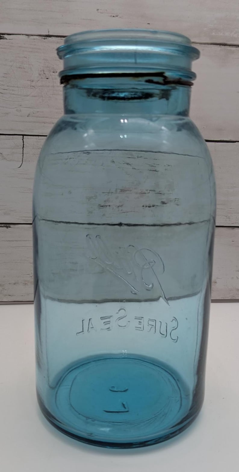 May include: A vintage blue glass jar with a matching lid. The jar has a wide mouth and a rounded body. The words "Sure Seal" are embossed on the front. A classic piece for storage or display.