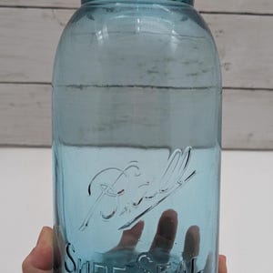 May include: A vintage blue Ball Sure Seal glass jar. The jar has a wide mouth and a screw-on lid. The Ball logo and "Sure Seal" are embossed on the front. The jar is held in a hand.