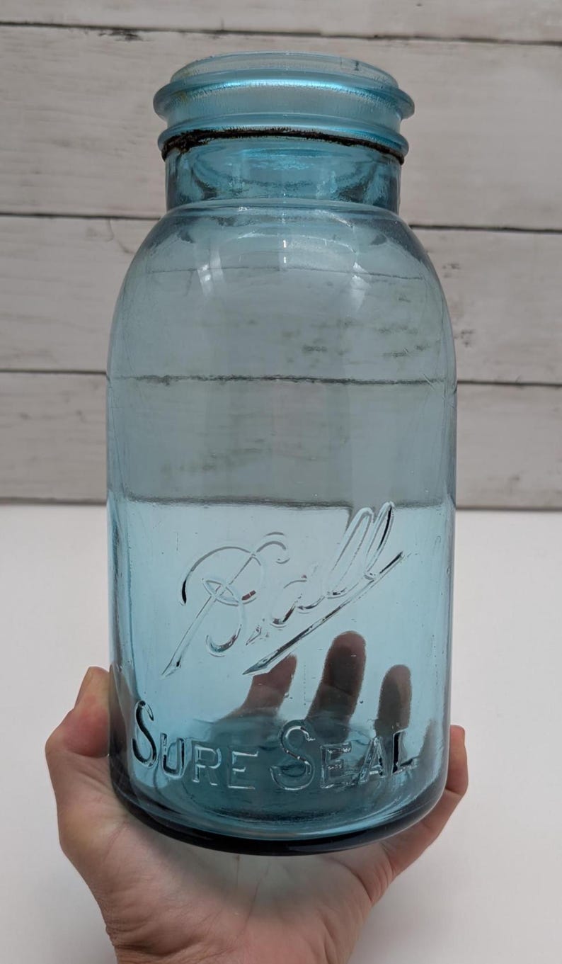 May include: A vintage blue Ball Sure Seal glass jar. The jar has a wide mouth and a screw-on lid. The Ball logo and "Sure Seal" are embossed on the front. The jar is held in a hand.