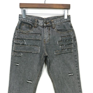 May include: Gray denim jeans with distressed details and patches featuring text like "HEART", "HUMAN", "BEASTITUDE", "ALTERNATIVE", and "SCRATCH".