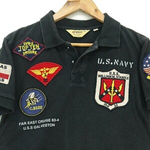 May include: Black short-sleeved polo shirt with multiple embroidered patches, including "U.S. Navy", "CVW-2 Top Ten", "C.Bees", "USS William M. Standle", and "Far East Cruise 63-4 USS Galveston".