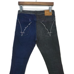 May include: A pair of dark blue and black denim jeans with a contrasting color split down the center seam. The jeans have a straight leg fit and a classic five-pocket design. The back pockets feature a white stitched design.