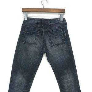 May include: A pair of dark blue denim jeans with a straight leg fit. The jeans have a zip fly and button fastening. The back pockets have a decorative stitching detail.