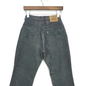 Puede incluir: Pantalones de pana gris oscuro con un diseño clásico de cinco bolsillos. Los pantalones se muestran en una percha, mostrando la vista trasera con el parche de la marca Levi's. La tela de pana tiene una apariencia texturizada.