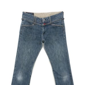 May include: Blue denim jeans with a distinctive waist design and flared, frayed hems. The jeans feature a button closure and a small red accent. The denim has a faded appearance.