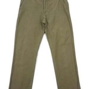 May include: Olive green pants with a button closure, belt loops, and front and back pockets. The pants are hanging on a wooden hanger against a white background. The pants are a solid color and appear to be made of a durable fabric.