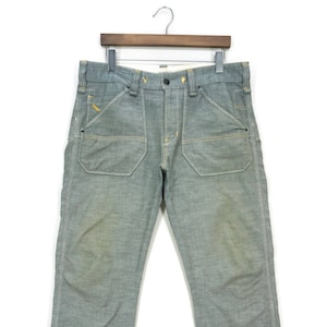 Puede incluir: Un par de pantalones vaqueros de mezclilla gris claro con un corte de pierna recta y un aspecto ligeramente descolorido. Los pantalones tienen cierre de botón y trabillas para cinturón.