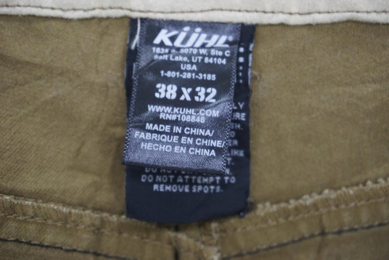 Puede incluir: Una etiqueta en blanco y negro con el nombre de la marca "K&Uuml;HL" y el texto "1634 0070 W, Ste C Salt Lake, UT 84104 USA 1-801-281-3185 38 x 32 WWW.KUHL.COM RN#108846 MADE IN CHINA/ FABRIQUE EN CHINE/ HECHO EN CHINA DO NOT ATTEMPT TO REMOVE SPOTS."