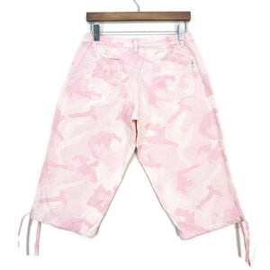May include: Pink camouflage print cropped pants with drawstring closures at the bottom of the legs.
