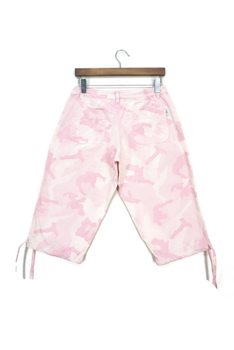 May include: Pink camouflage print cropped pants with drawstring closures at the bottom of the legs.