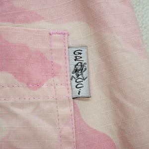May include: Pink camouflage fabric with a white label that says "Gelato" with a graphic of a person in a circle.
