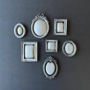 Op de afbeelding: Set van zeven zilverkleurige fotolijsten met sierlijke details. De lijsten zijn in verschillende maten en vormen, waaronder ovaal, vierkant en rechthoekig.