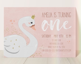 May include: A pink invitation card with a swan illustration and the text "Amelia is turning one." The card includes event details: date, time, and location. Gold glitter accents and a crown on the swan add a touch of elegance. The text "free white envelope included" is at the top.