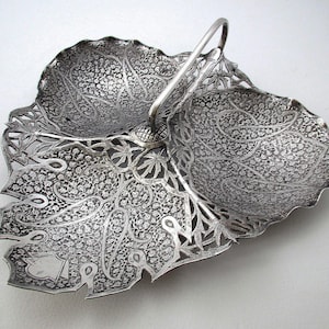 May include: A silver serving dish with a handle in the shape of a leaf. The dish is intricately decorated with a floral pattern.