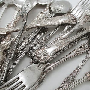 May include: A collection of antique silver-plated cutlery, including forks and spoons, featuring elaborate floral and scroll patterns. The close-up image highlights the detailed designs and reflective surfaces of the silverware.