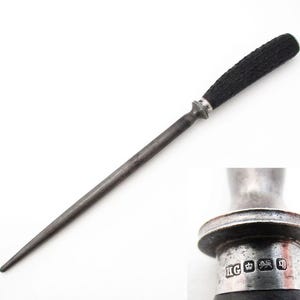 Könnte beinhalten: Ein Vintage-Stahl-Messerschärfer mit einem strukturierten schwarzen Griff und einem silbernen Metallansatz. Der Schärfer ist lang und schlank, mit einer spitzen Spitze. Der Griff scheint aus einem dunklen, möglicherweise natürlichen Material zu bestehen.