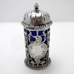 以下が含まれることがあります： 透かし彫りの蓋と装飾的なフィリグリーデザインが施された銀製の砂糖入れ。内部は鮮やかな青色です。砂糖入れには装飾的なつまみと、ボディに施された詳細な彫刻模様があります。砂糖をサーブするためのクラシックなアイテムです。