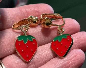 May include: Clip-on earrings featuring a red strawberry design with green leaves and gold-colored metal accents. The earrings have a clip-on mechanism for easy wear.