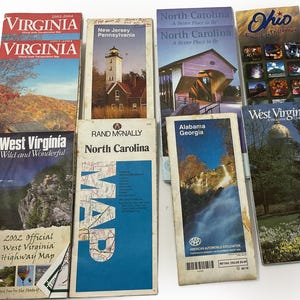 May include: A collection of eight folded paper state highway maps featuring various US states including Virginia, New Jersey, Pennsylvania, North Carolina, Ohio, West Virginia, Alabama, and Georgia, each displaying colorful landscape photography and text.