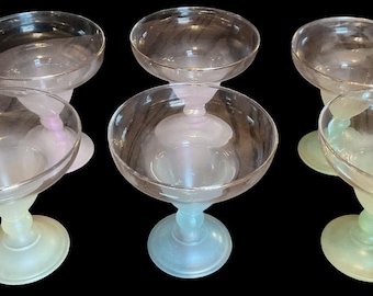 May include: Six clear glass dessert or cocktail glasses with rounded bowls and short stems. The stems transition from a pale green to a clear base. The glasses are arranged on a black background.