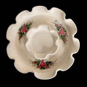 以下が含まれることがあります： クリーム色のセラミック製サービング皿。縁はスカラップで、中央には小さな皿があります。手描きのピンクのバラ、緑の葉、赤いベリーで飾られています。全体的なデザインは花のテーマです。