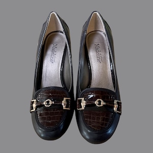 May include: A pair of black leather heeled loafers with a brown crocodile-textured vamp. The shoes have gold-coloured hardware and the brand name "Madeline" is visible inside.