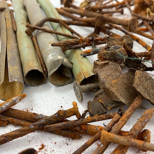 May include: A collection of weathered metal components including several hollow, cylindrical tubes with a pale green finish and a large assortment of rusted iron nails and fragments scattered across a flat surface with visible oxidation.
