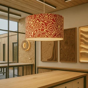 May include: A cylindrical pendant lamp with a red and cream-colored organic pattern hangs from the ceiling. The lamp is the focal point of a room with wooden tables and decorative wall panels.