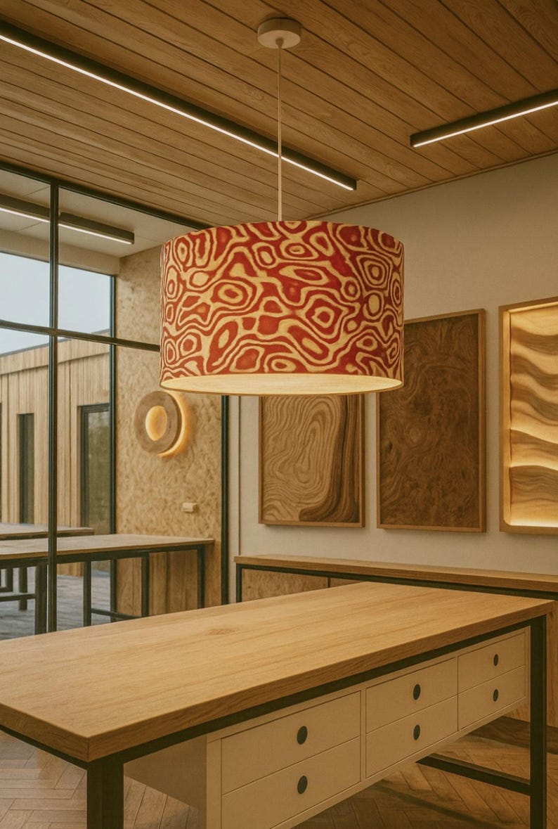 May include: A cylindrical pendant lamp with a red and cream-colored organic pattern hangs from the ceiling. The lamp is the focal point of a room with wooden tables and decorative wall panels.