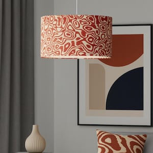 May include: A red and cream-colored pendant lamp with a swirling pattern hangs from the ceiling. A matching throw pillow rests on a gray sofa. A framed abstract art print and a vase are also visible.