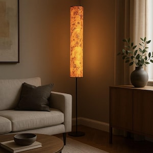 May include: A tall, cylindrical floor lamp with a black metal base and a textured, amber-colored shade. The shade has a mottled pattern, and the lamp is illuminated, casting a warm glow. The lamp is in a living room setting.