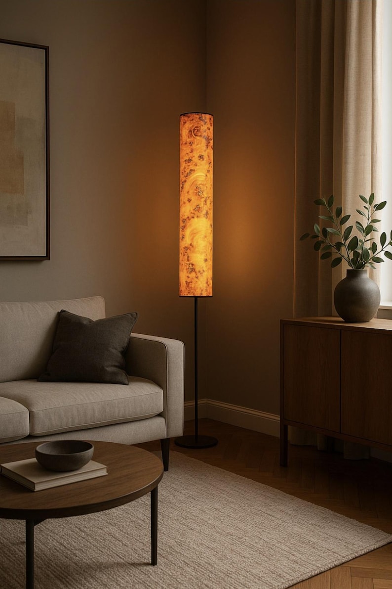 May include: A tall, cylindrical floor lamp with a black metal base and a textured, amber-colored shade. The shade has a mottled pattern, and the lamp is illuminated, casting a warm glow. The lamp is in a living room setting.