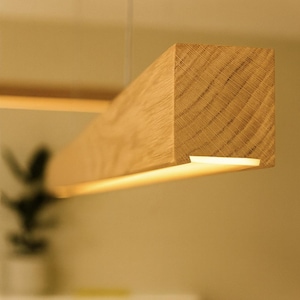 May include: A rectangular wooden light fixture with a warm, yellow glow. The fixture is made of light-colored wood and is suspended from the ceiling. The wood grain is visible, adding texture to the design. The light is on, illuminating the space below.