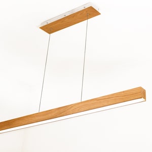 May include: A modern, rectangular pendant light fixture. The light features a long, wooden beam with a bright, white light strip. The fixture is suspended by thin, silver cables from a rectangular wooden ceiling mount.