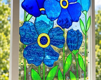 May include: A rectangular window panel featuring a stained glass style design of blue flowers with yellow centers and green stems. The petals display various textures including swirls and dots, framed in a white border against a clear glass background.