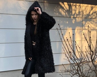 May include: A black fuzzy hooded cardigan with a long sleeve and a black top underneath. The person is wearing black leggings and black ankle boots.