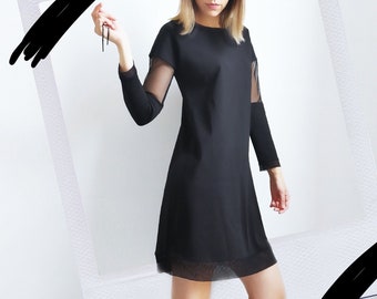 Peut inclure: Une femme portant une robe noire avec des manches transparentes et des sandales à plateforme noires à lacets. Elle se tient devant un mur blanc avec un cadre photo noir et blanc.