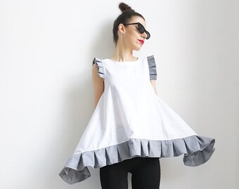 May include: A white sleeveless top with a gray ruffle trim and black leggings. The top has a loose, flowing fit and the leggings are fitted. The person is wearing black platform sandals with laces.
