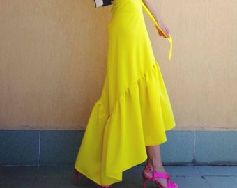 May include: A woman wearing a black and white striped crop top and a bright yellow, asymmetrical skirt with a ruffle hem. She is wearing pink high heels.