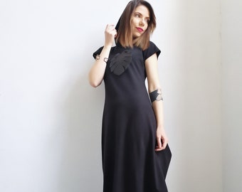May include: A black maxi dress with a hood and a large leaf design on the front. The dress has short sleeves and a loose fit.