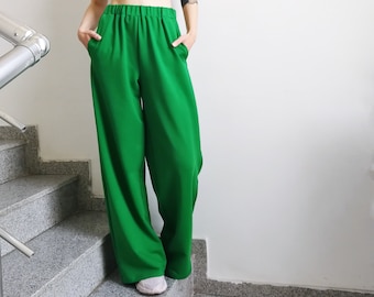 May include: A woman wearing a black crop top and wide-legged green pants. She is standing on a set of stairs.