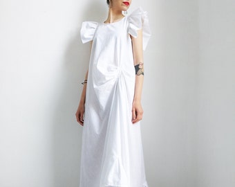 May include: A white maxi dress with ruffled sleeves and a gathered skirt. The dress has a simple, elegant design and is perfect for a summer occasion.