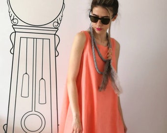 May include: A woman wearing a coral sleeveless dress with a gray rope necklace and feather accents. She is wearing rose gold sneakers with a bow.