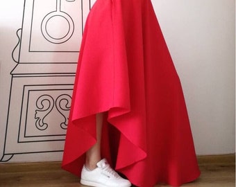 May include: A woman wearing a white t-shirt with the word "minimal" printed on it, and a red high-waisted skirt with a high-low hemline. The skirt is flowing and has a slight A-line shape. She is wearing white sneakers.