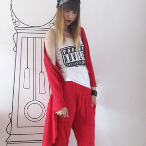 Peut inclure: Une femme portant une tenue rouge avec un t-shirt blanc sur lequel est inscrit "Parental Advisory" en lettres noires. Elle porte un bandana noir et des baskets blanches.