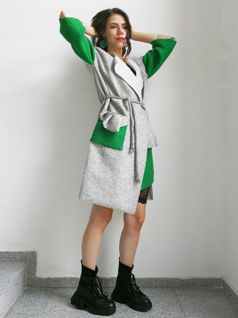 May include: A gray and green cardigan with a white collar and a tie belt. The cardigan has a large patch pocket on the front. The model is wearing black boots.