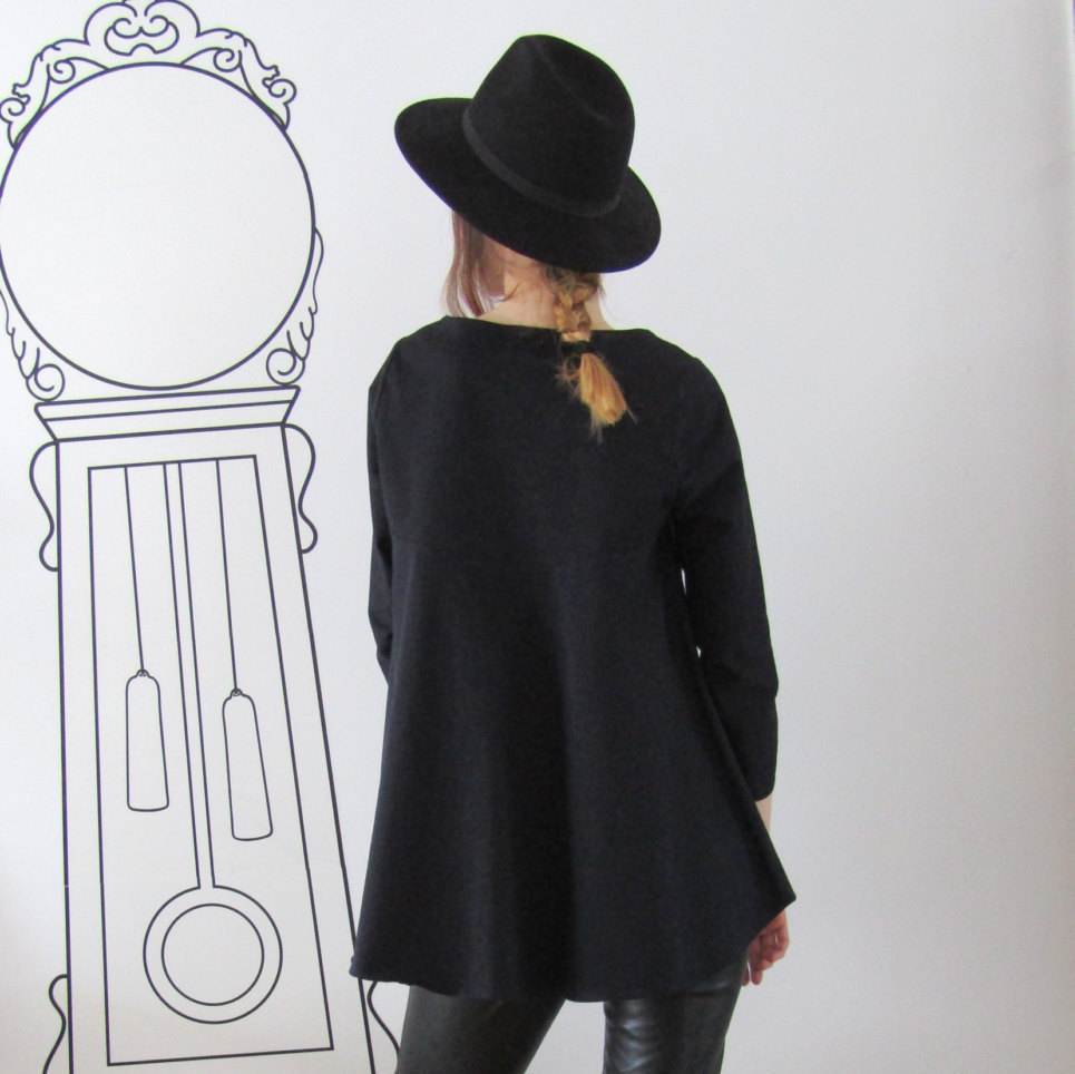 May include: A black long-sleeved tunic with a wide, flowing hemline. The tunic is worn with black pants and a black fedora hat.